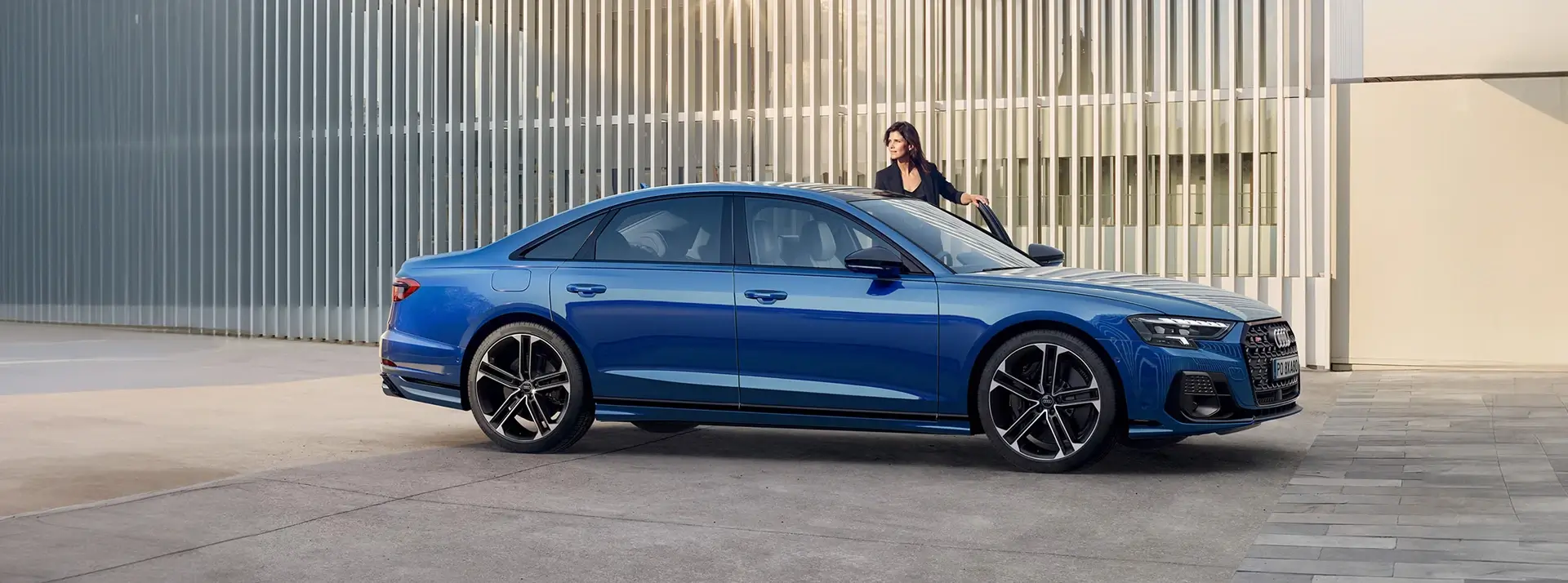 kobieta wysiadająca z ciemnoniebieskiego Audi A4 zaparkowanego przed nowoczesnym budynkiem