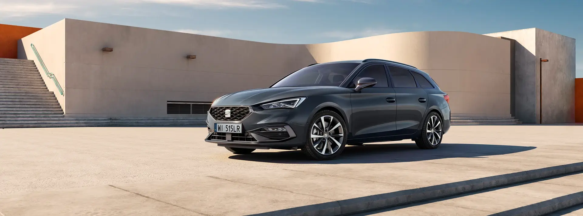 SEAT Leon Sportstourer w kolorze grafitowym, stoi na tle niskich piaskowch budynków