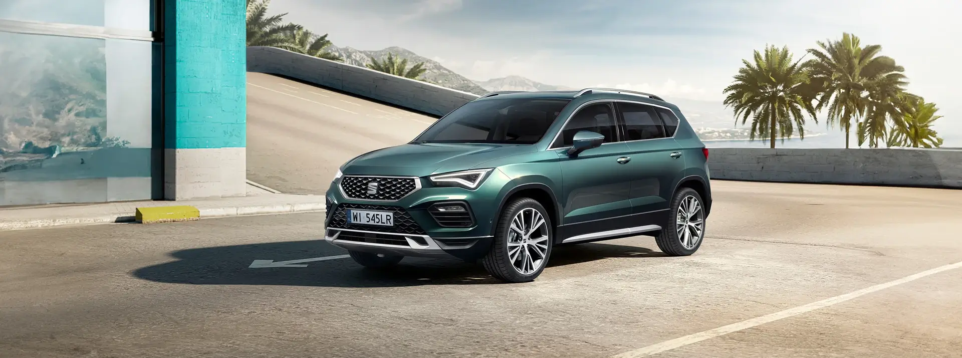 zielony SUV SEAT Ateca na tle nowoczesnego budynku, morza i palm