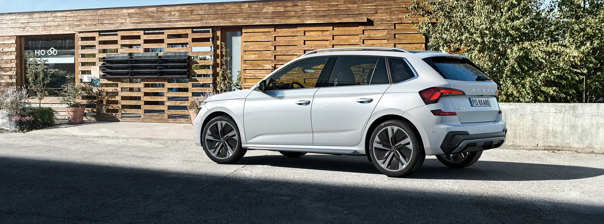 biała Skoda Scala na tle niskiego budynku z drewnianą elewacją