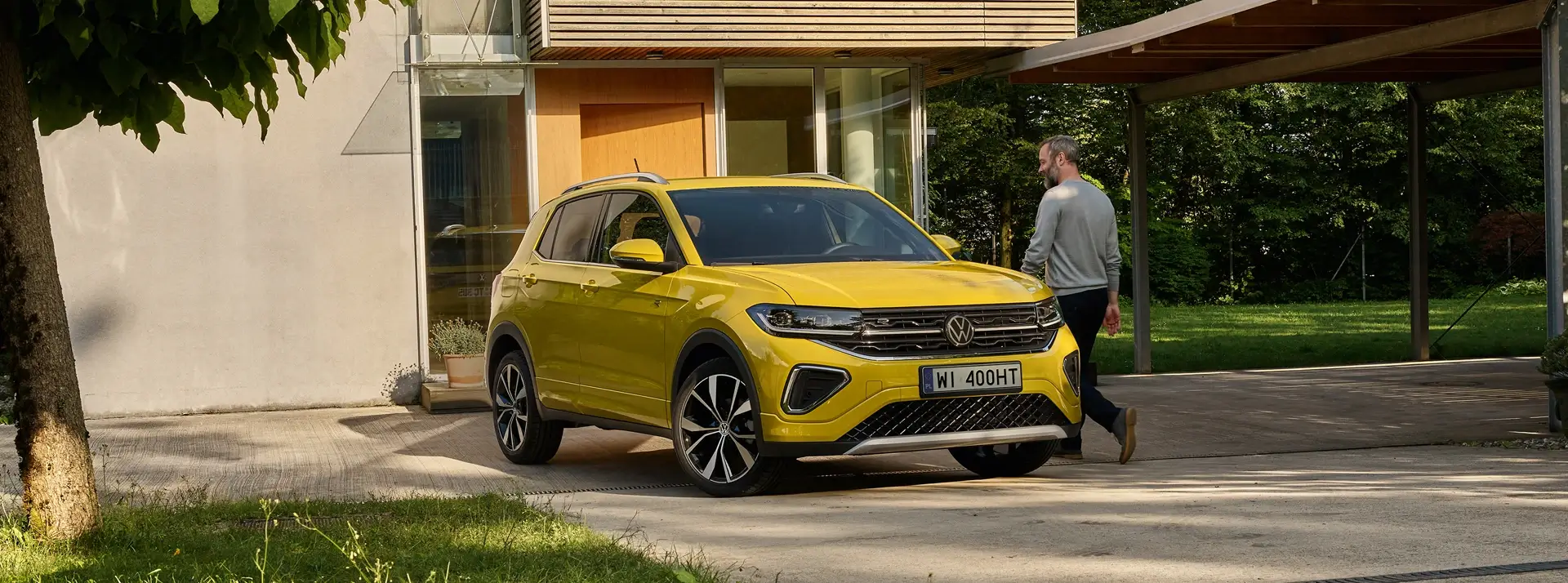 mężczyzna w średnim wieku przy żółtym crossoverze Volkswagen T-Cross, w tle nowoczesny dom jednorodzinny
